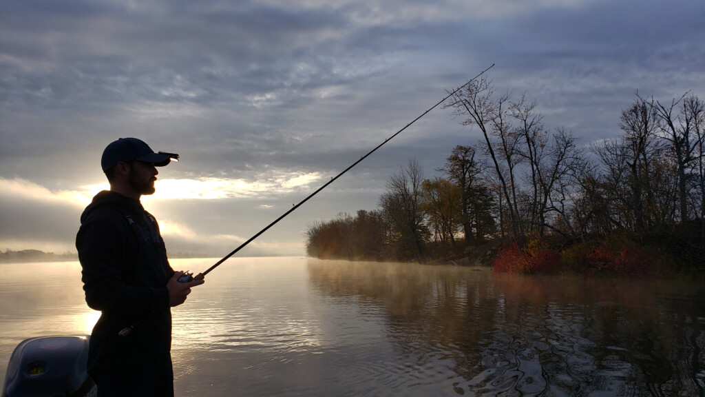 Man holding fishing rod over river after sunset 