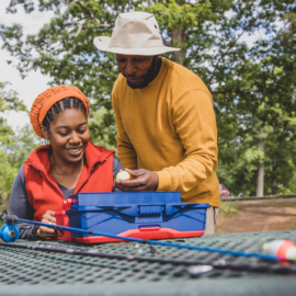 A couple of anglers look through a tackle box on a picnic table.