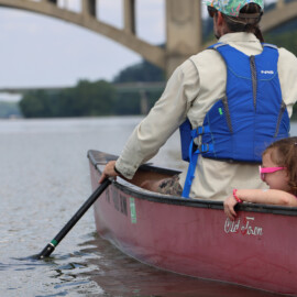 Man and young girl both wearing life jackets while canoeing along the Susquehanna River.
