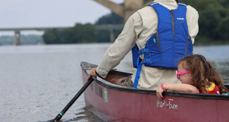 Man and young girl both wearing life jackets while canoeing along the Susquehanna River.