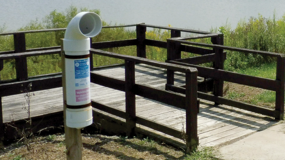 A fishing line recycling tube next to a pier on a lake.