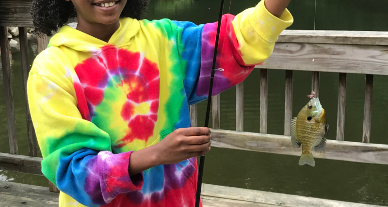 A girl poses for a photo after catching a panfish.