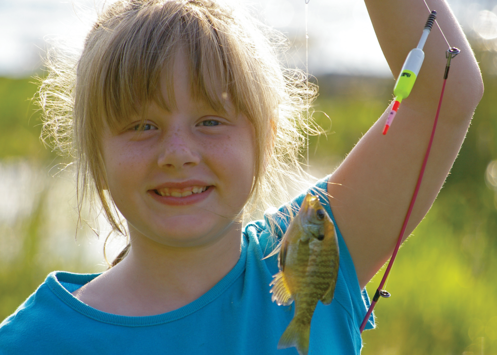 A young angler poses for a photo with a panfish on the end of her fishing line.