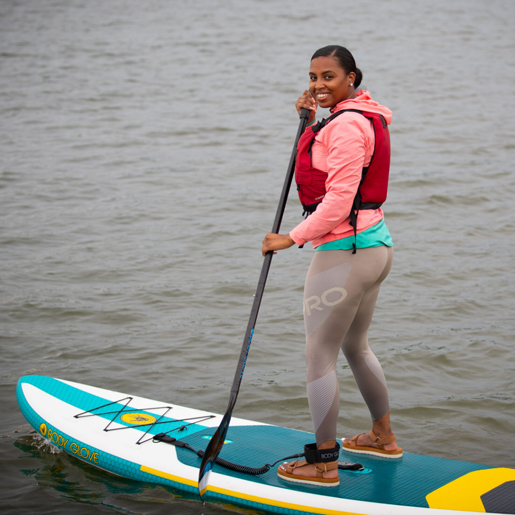 A person wearing a life jacket paddles while standing on a stand-up paddleboard.