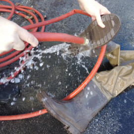 A person uses a garden hose to wash off the boots of his waders.