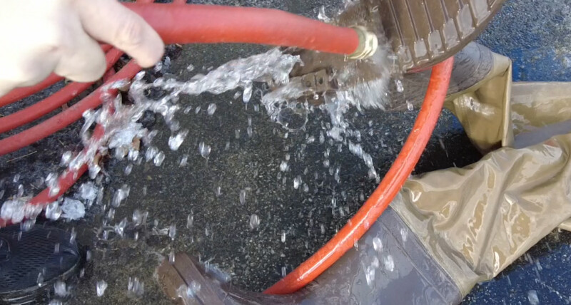 A person uses a garden hose to wash off the boots of his waders.