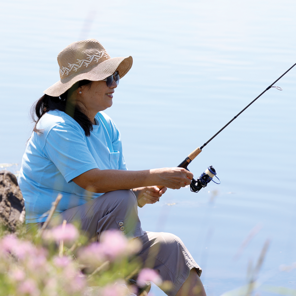 A woman fishing from shore on a lake.