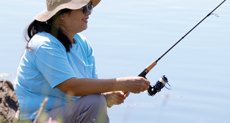 A woman fishes from shore on a lake.