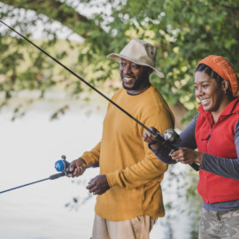 Man and Woman fishing along lakeshore lined with trees