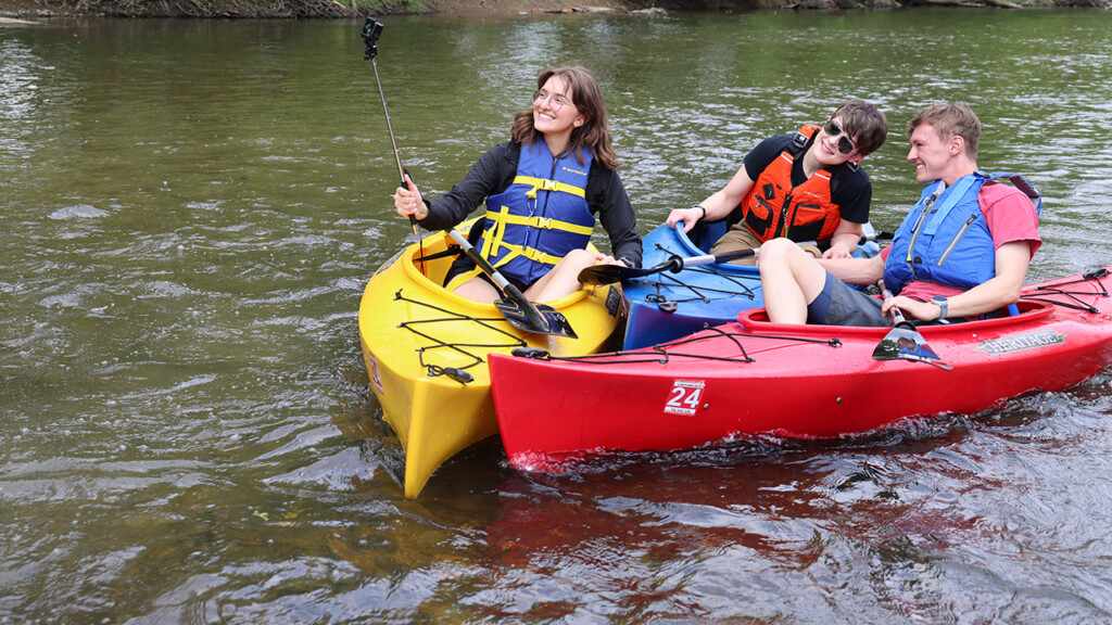 Three kayakers taking a selfie photo on the water 