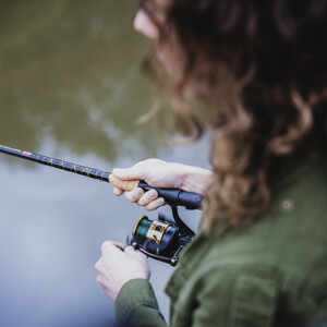 View of a woman fishing along a streambank from over her shoulder