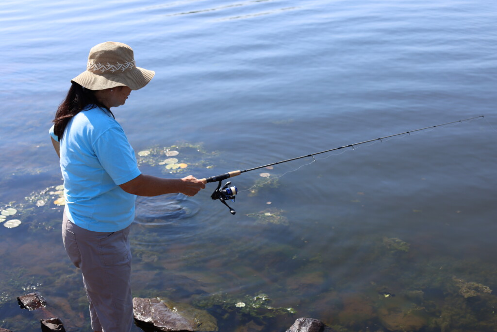 Woman fishing on shore with summer hat on her head 