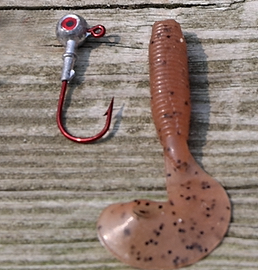 A red Medium Round Head Jig with an eye at the top of the hook sitting next to a spotted red Twister Tail lure for imitating aquatic critters