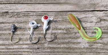 Three Small Round Head Jig with an eyes at the top of the hooks sitting next to a small Curly Tail lure used for imitating small macroinvertebrates.