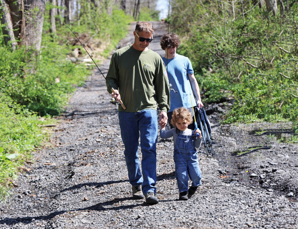 A grandfather, son, and grandson, carrying fishing gear, hike to a fishing spot in Tyler State Park to 