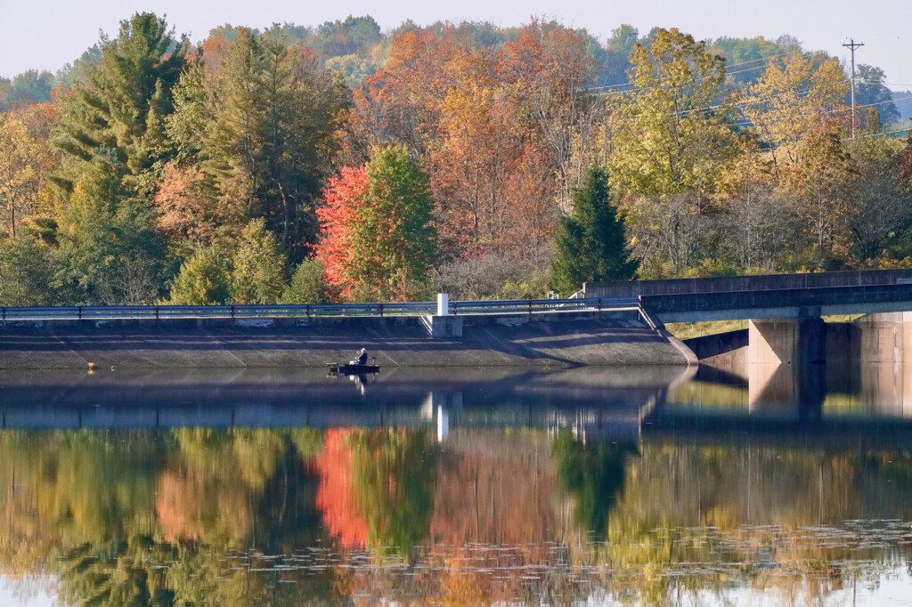 Wide shot of a person kayaking on Hills Creek Lake in Hills Creek State Park with fall foliage in the background