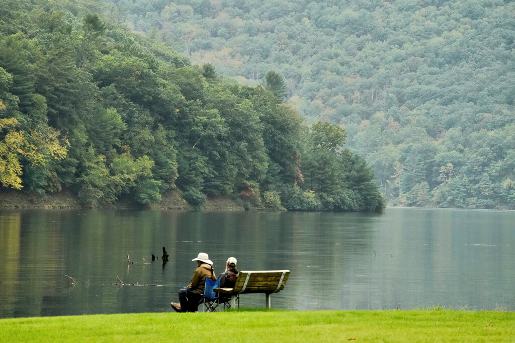 Couple sitting on a park bench admiring the view of the lake at Kettle Creek State Park with greenery in background.