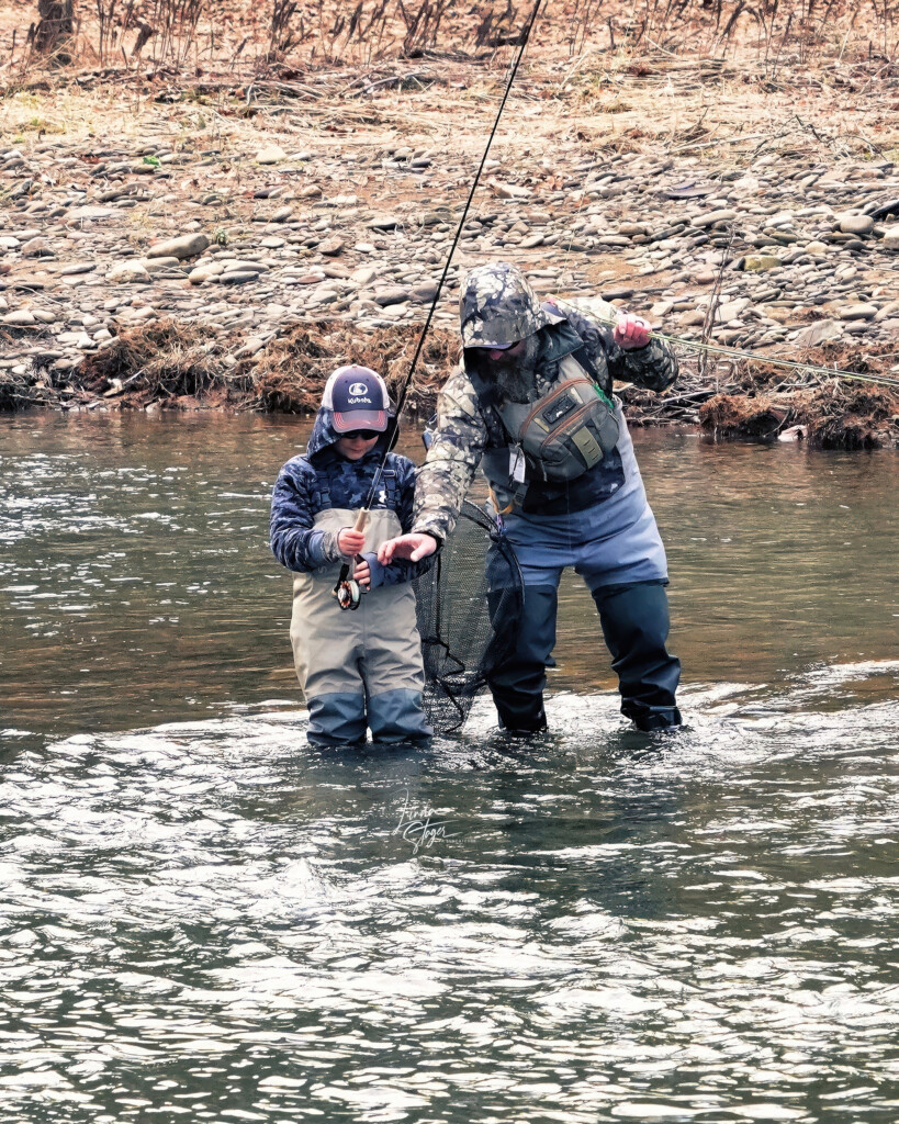 Man and young child wading in a stream and fixing their fishing rods.