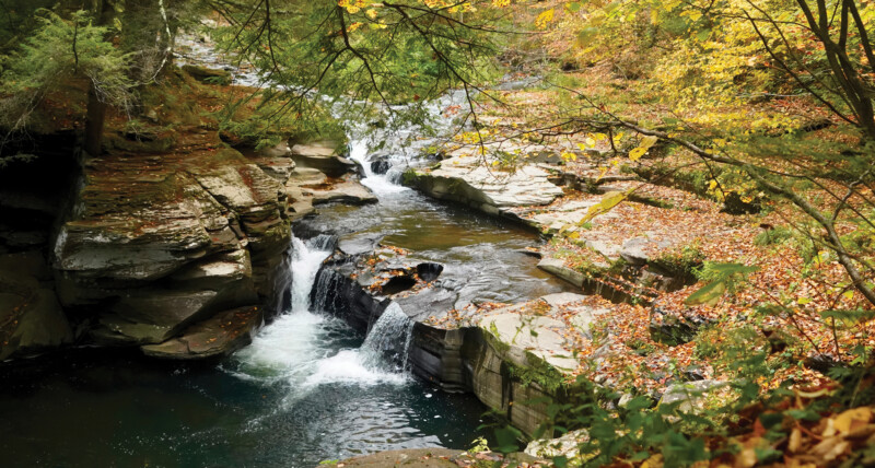 Scenic photo of a small rocky waterfall surrounded by green scenery.