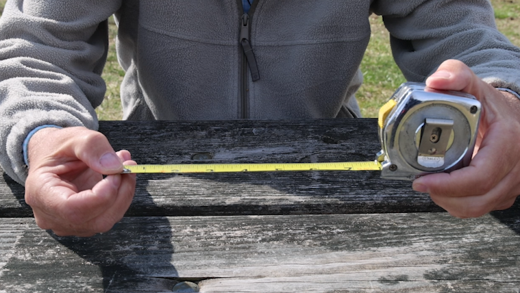 Man's hands opening a tape measure to 7 inches