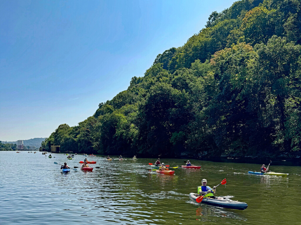 Group of sojourn paddlers on one of the Three Rivers with scenic forestry in the background.