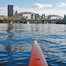Tip of a long river kayak overlooking a beautiful, scenic view of the Pittsburgh skyline.